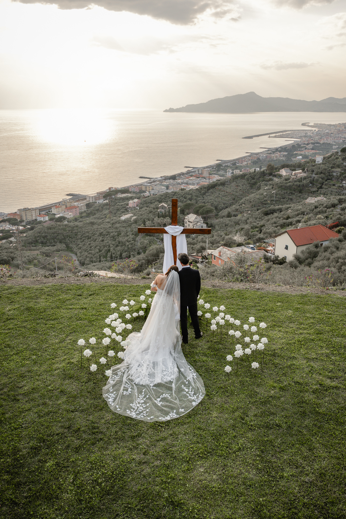 Christian wedding ceremony in Italy with bride and groom praying at cross overlooking the sea, destination wedding Italy