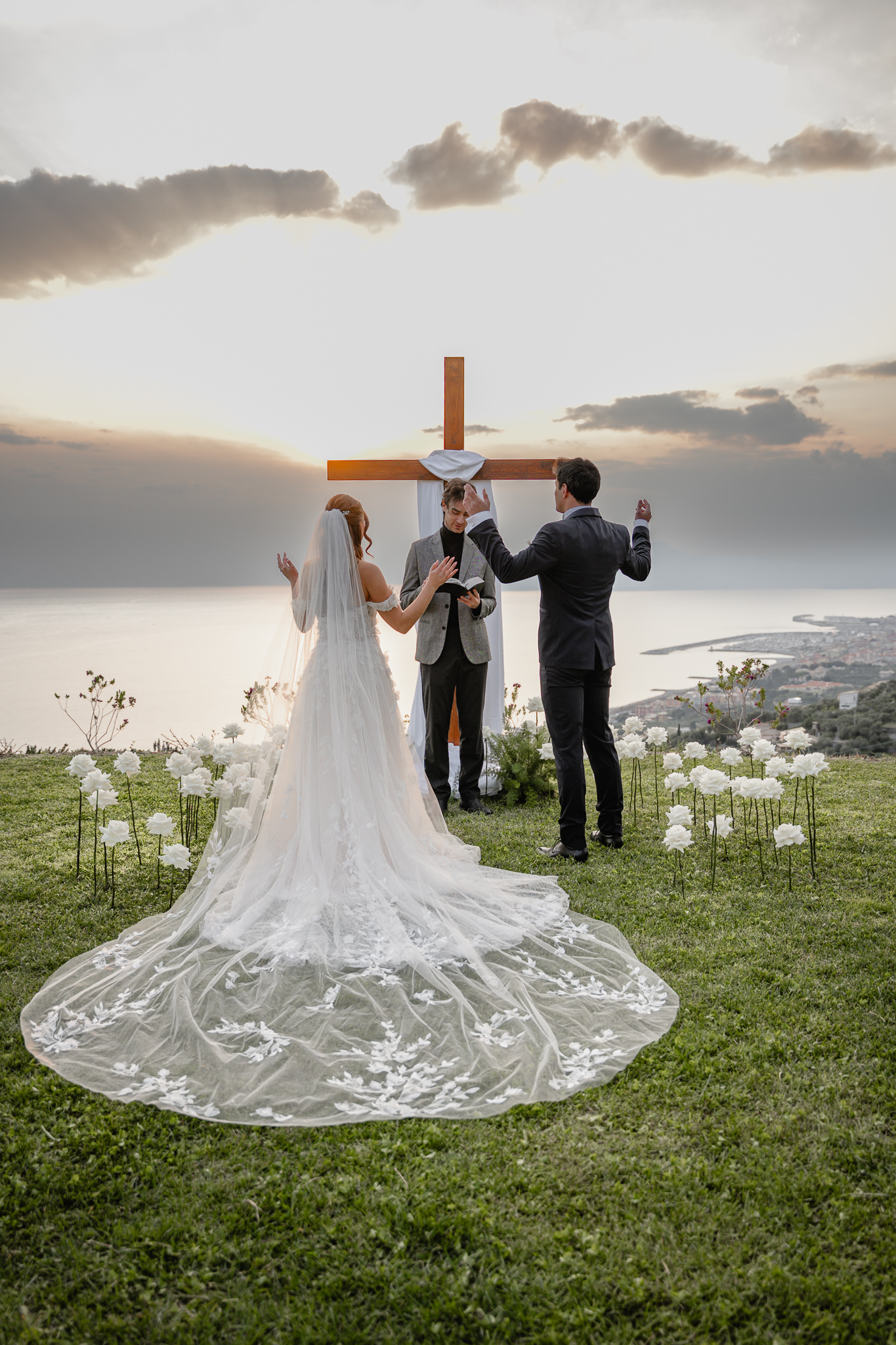 Bride and groom praying with raised hands during a Christian destination wedding in Italy, pastor reading the Bible at sea view ceremony