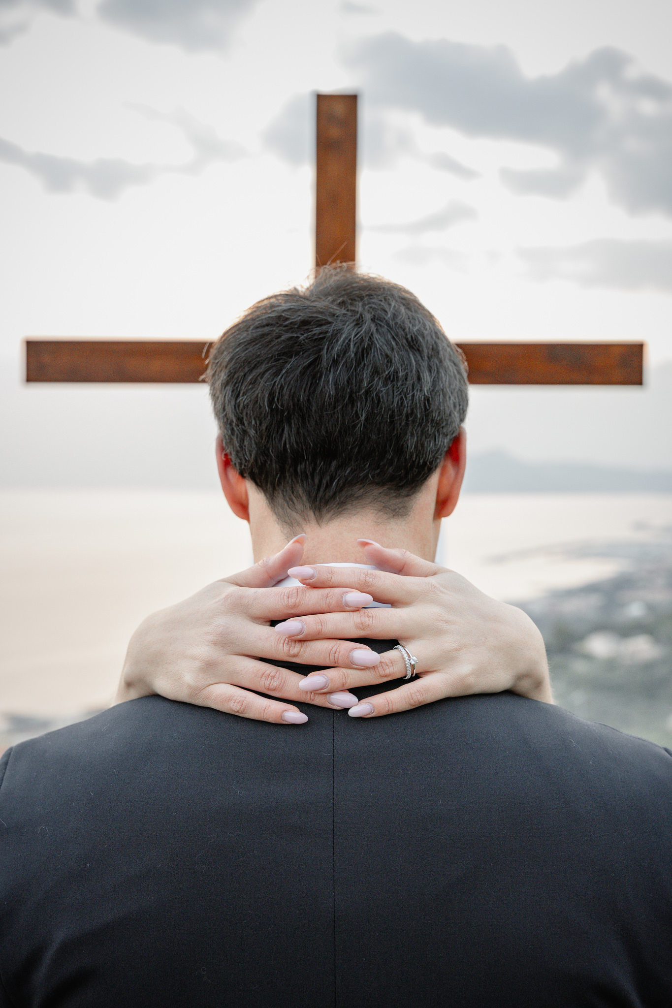 Bride holding groom with wedding rings visible during a Christian destination wedding in Italy, cross and sea view ceremony setting